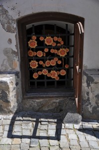 Zamrežované pivničné okno starobylého domu s povešanými keramickými slniečkami.